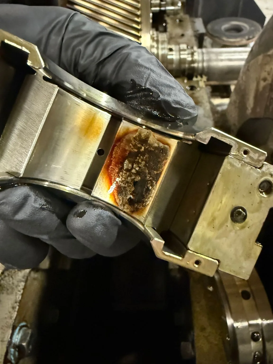 Gloved hand holding a worn journal bearing pad removed from the Joy TA-50